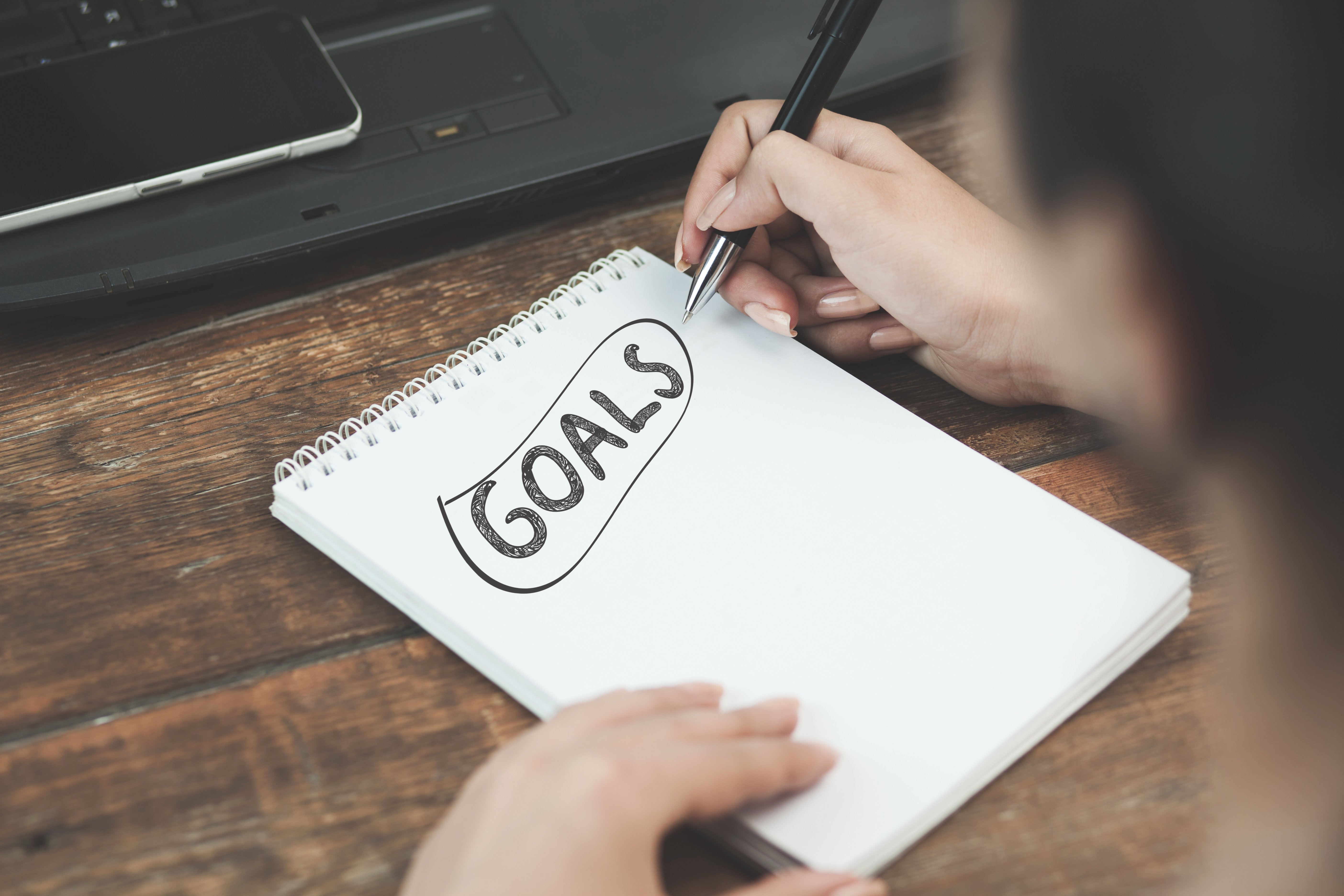 person writing down their goals on a notepad